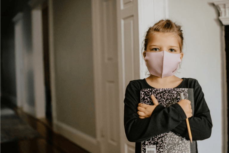 Kind mit Maske und Schreibwahren